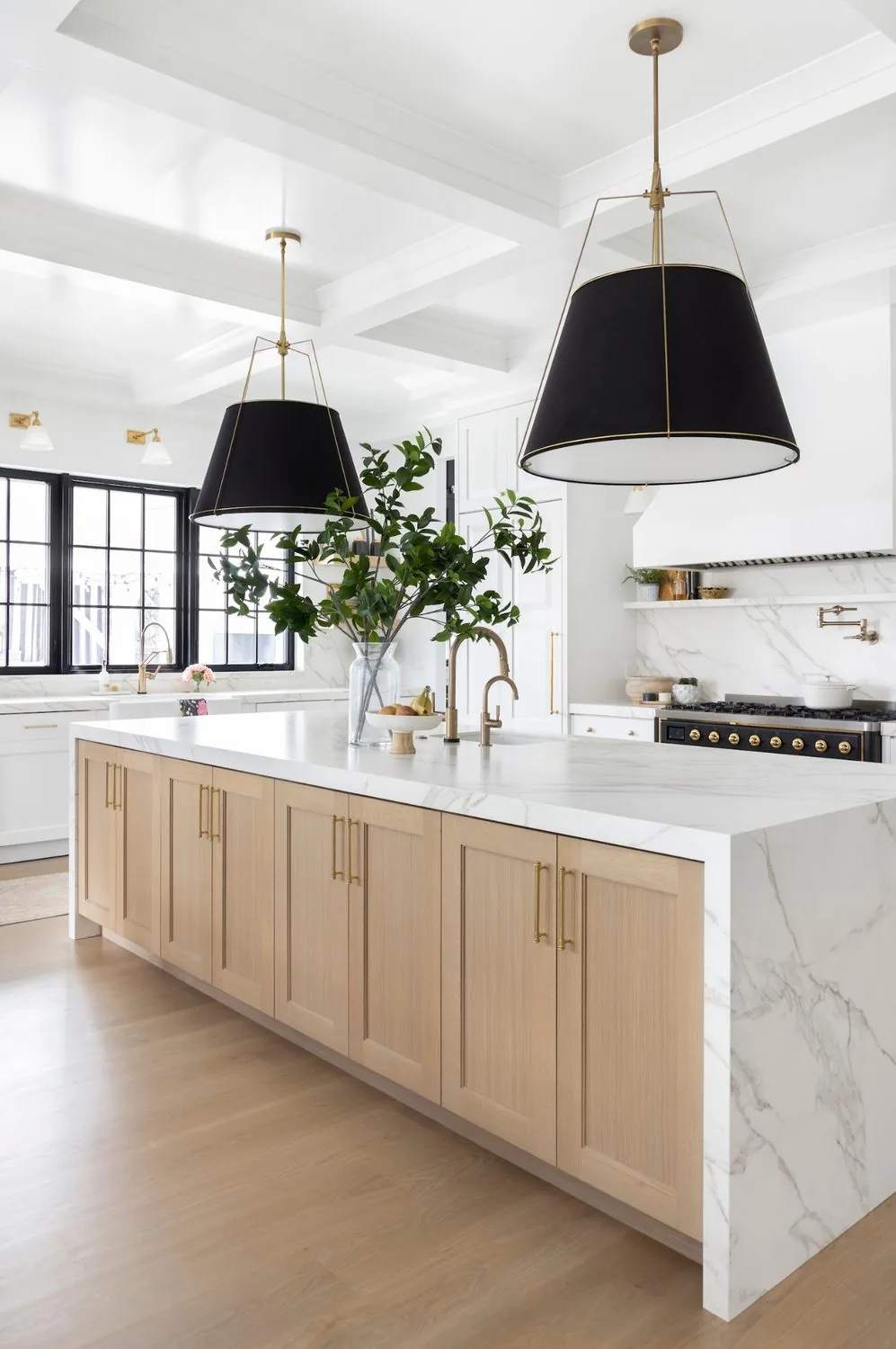 Kitchen with an oak island, stone waterfall counter and black shaded pendants