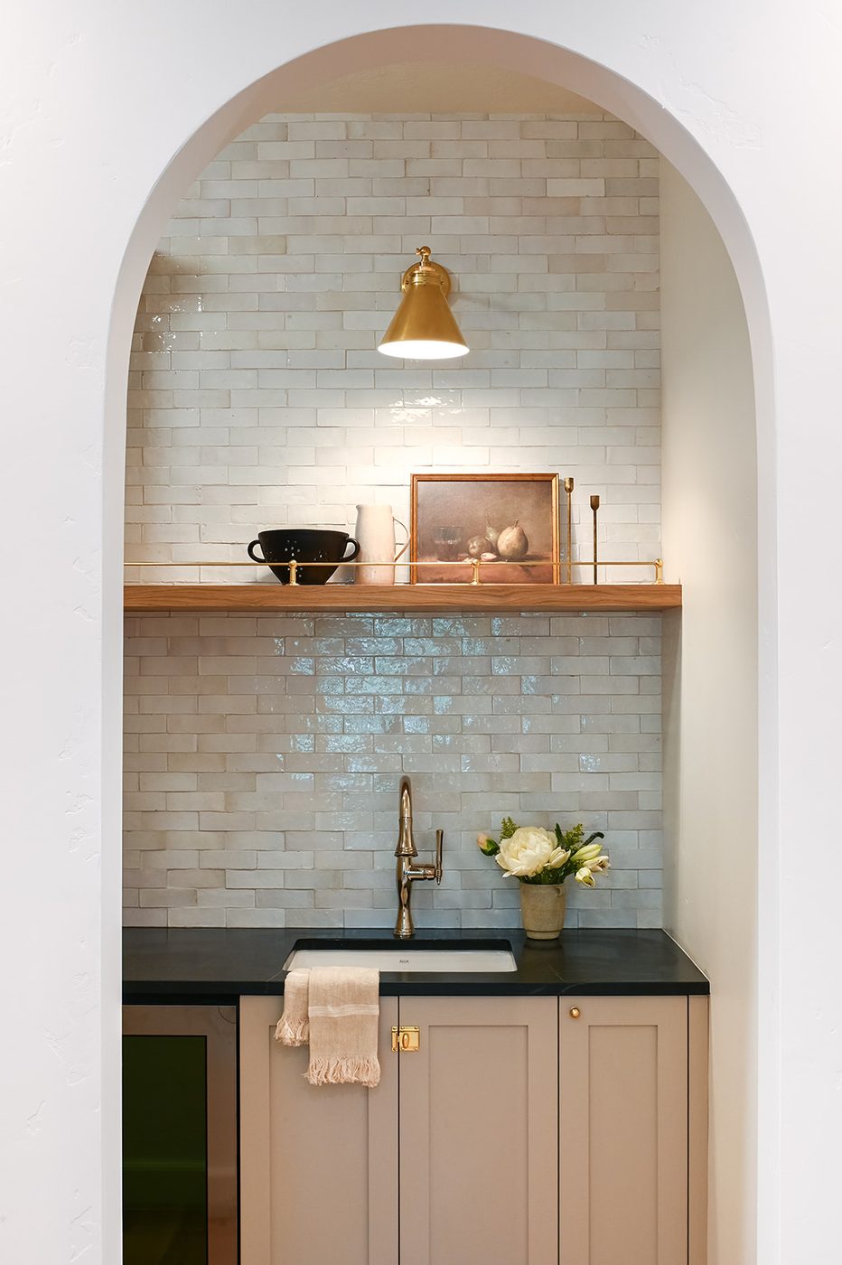 Arched pantry nook with handmade glazed tile, an oak shelf and a brass sconce