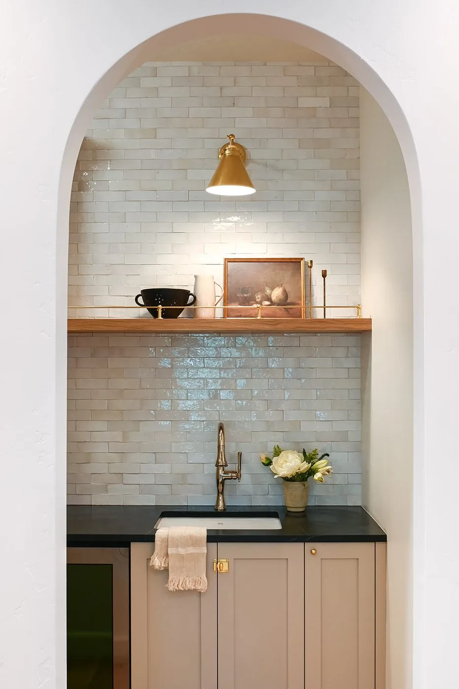Arched pantry nook with handmade glazed tile, an oak shelf and a brass sconce
